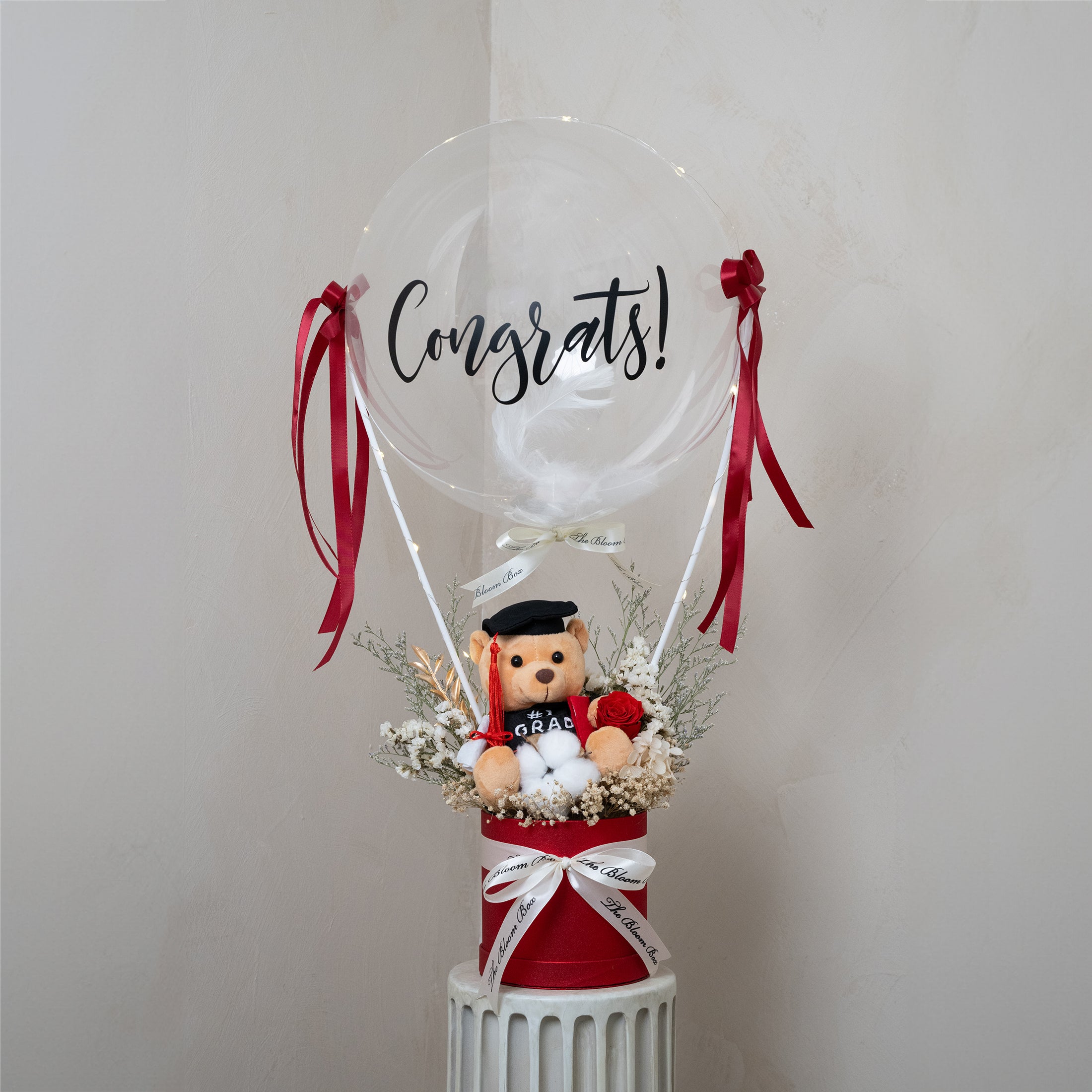 grad bear in red box with red preserved flower arrangements and congrats message balloon decorated with fairy light