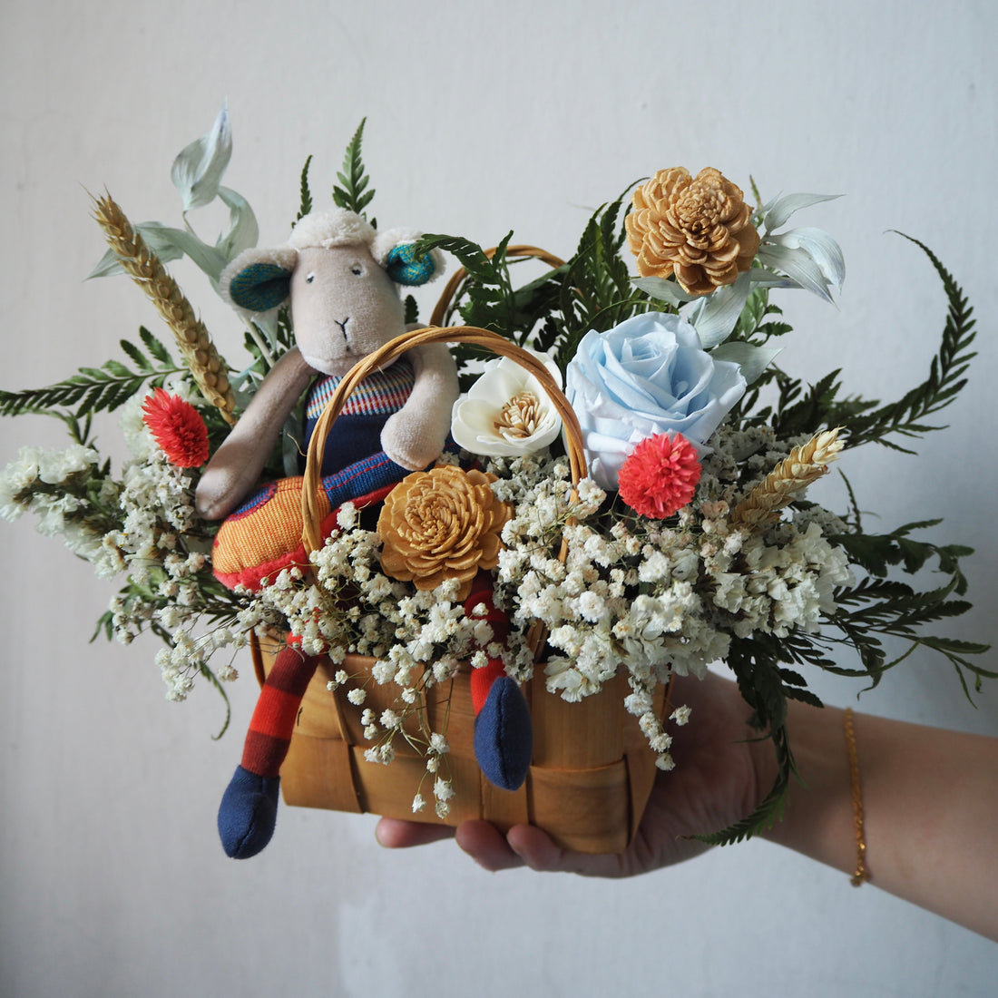 Hand holding a bouquet with a small toy figure inside, surrounded by flowers and greenery.