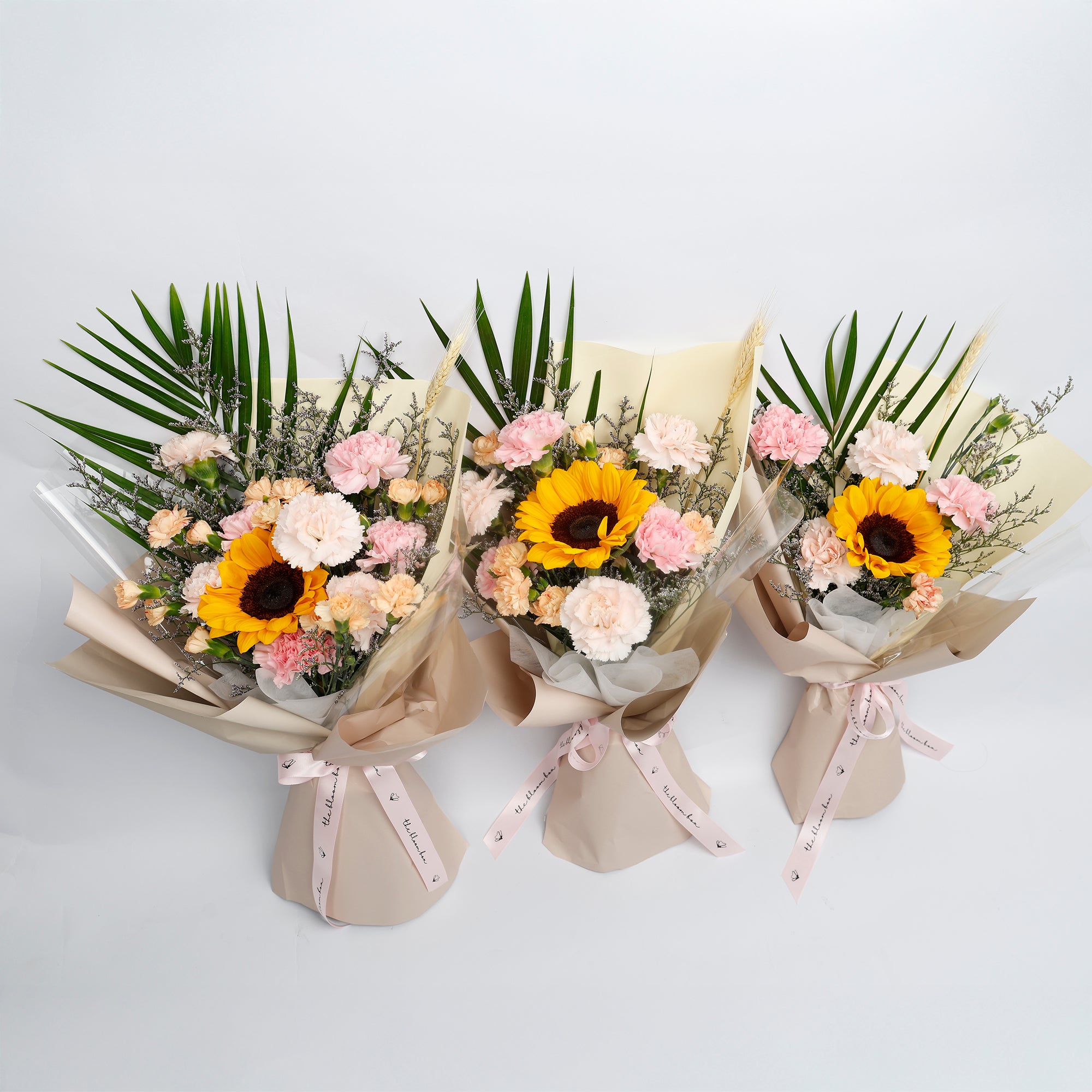 Three flower bouquets with sunflowers and pink flowers on a light gray background