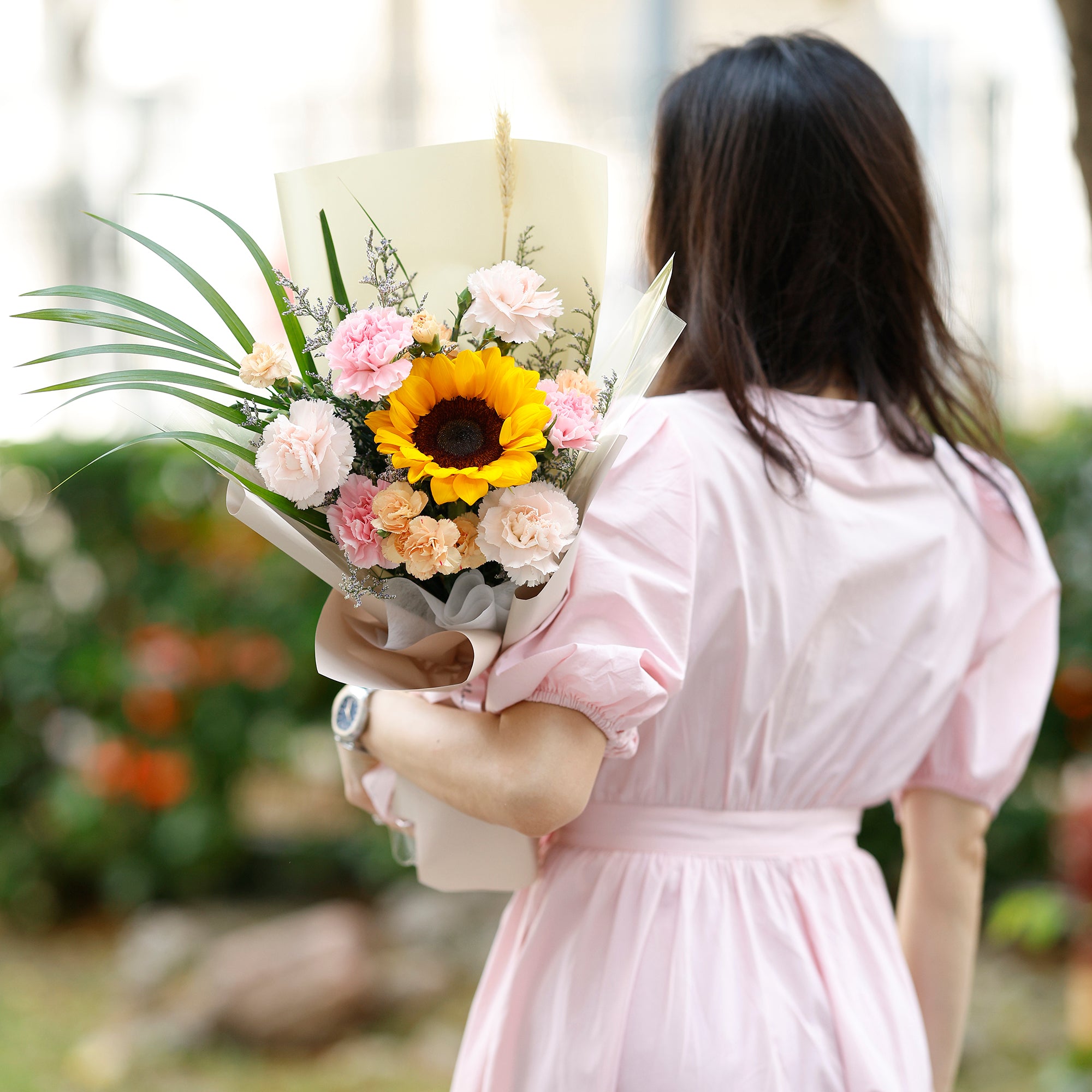Woman in a pink dress holding a bouquet of flowers outdoors