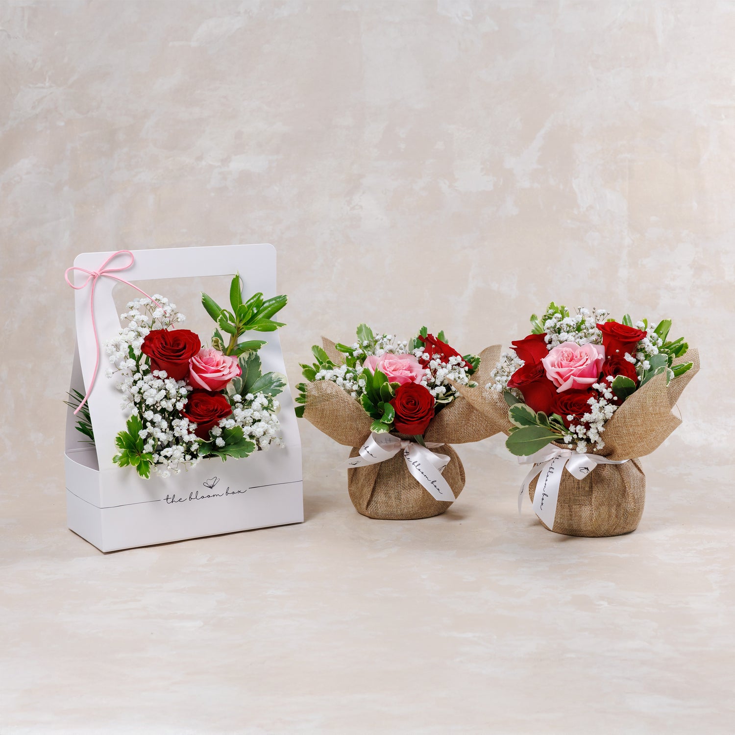 Three small flower bouquets in burlap bags and a box on a light background