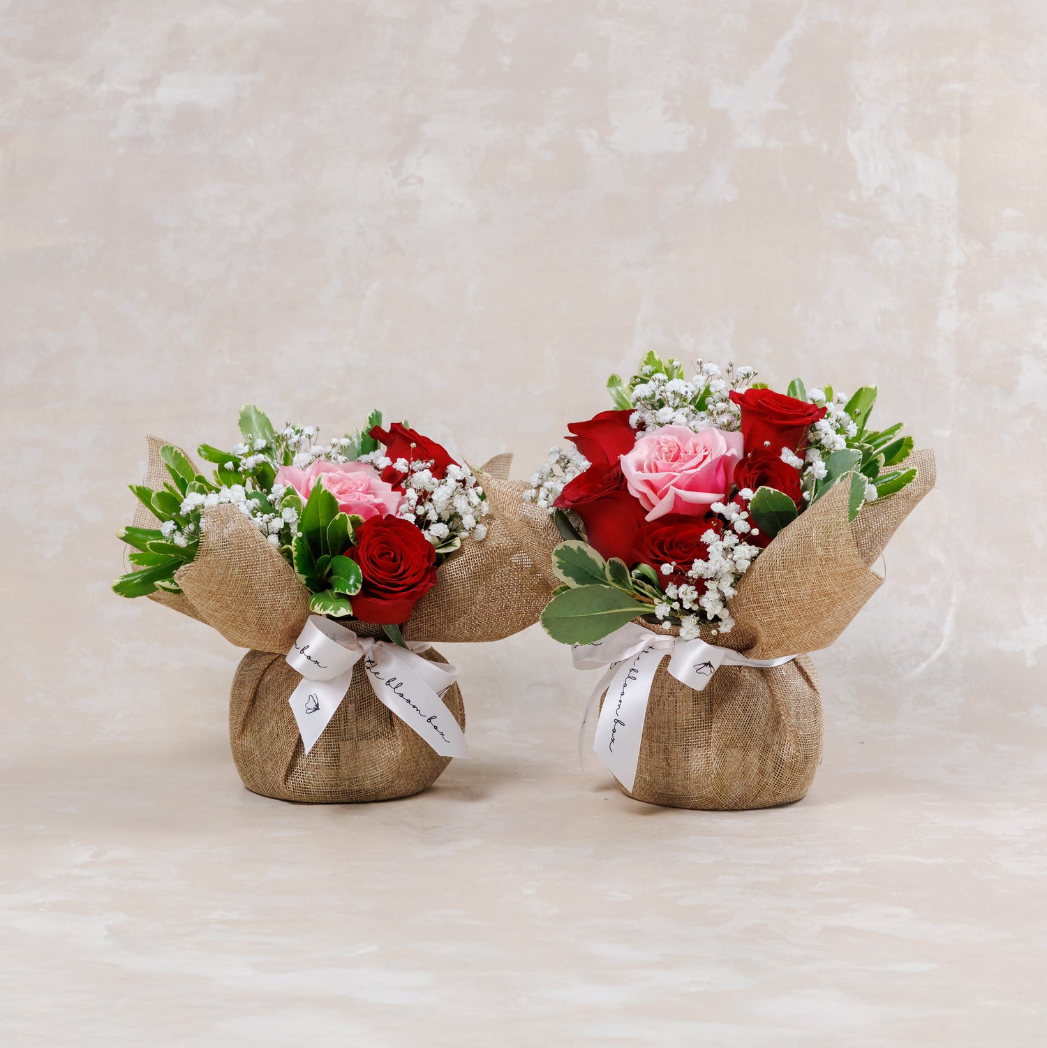 Two small flower bouquets wrapped in burlap on a beige background