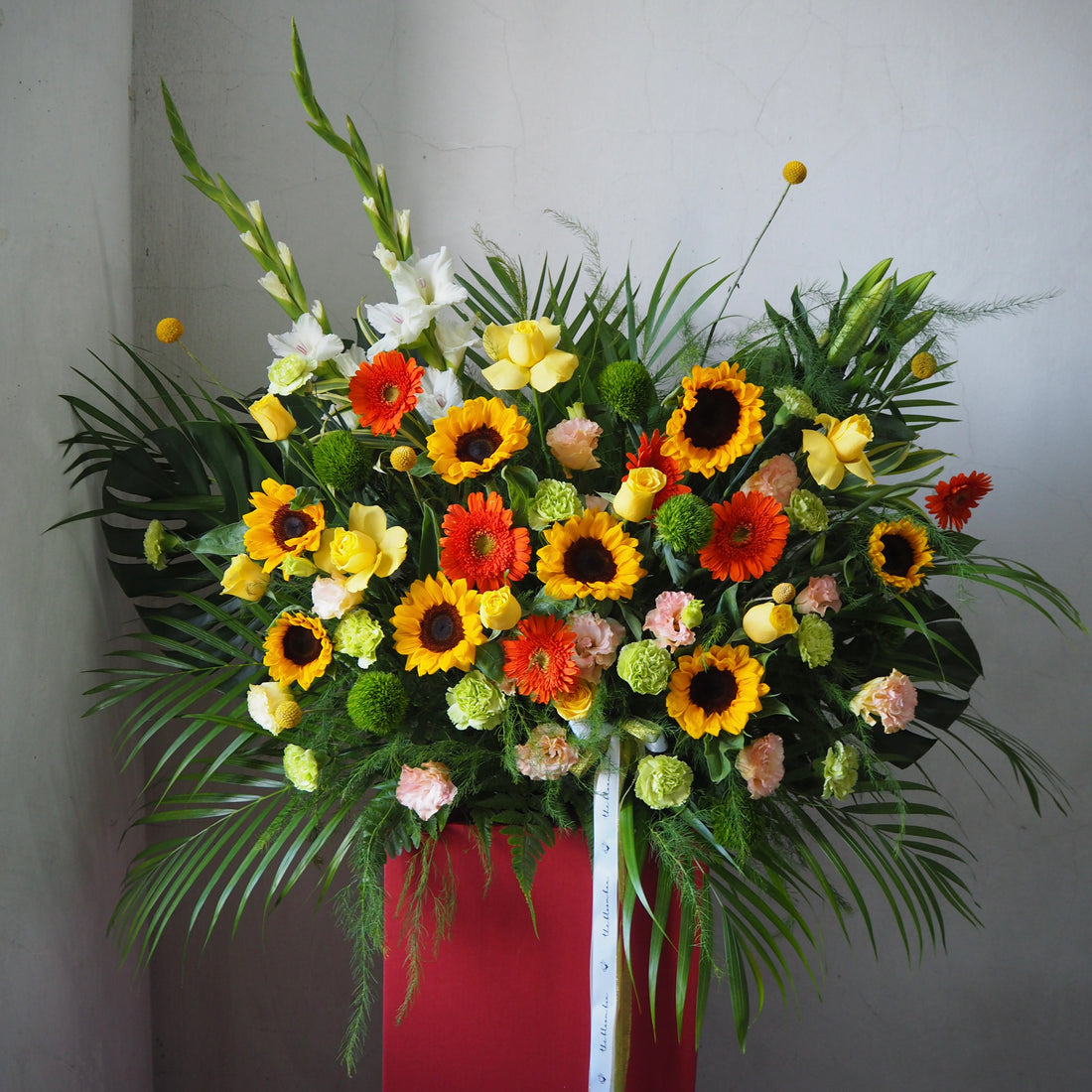 Colorful flower arrangement with sunflowers and other flowers on a red stand against a plain background