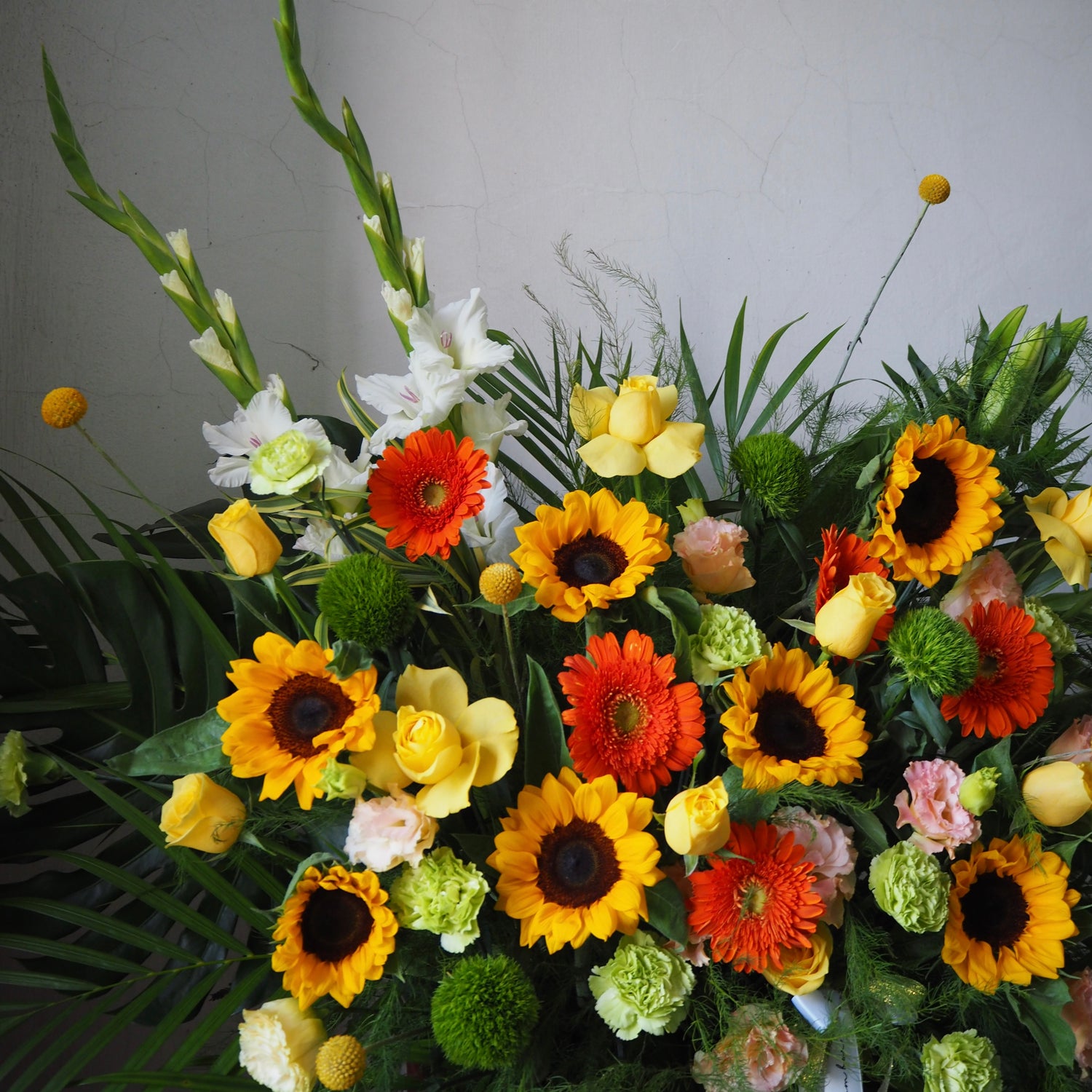 Bouquet of colorful flowers including sunflowers, roses, and daisies against a neutral background.
