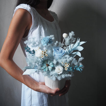 lady holding light pale blue preserved flower arrangements in white strip vase