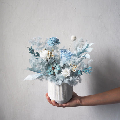 light pale blue preserved flower arrangements in white strip vase