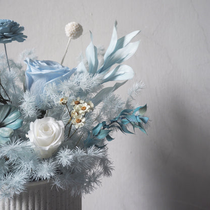 close up light pale blue preserved flower arrangements in white strip vase