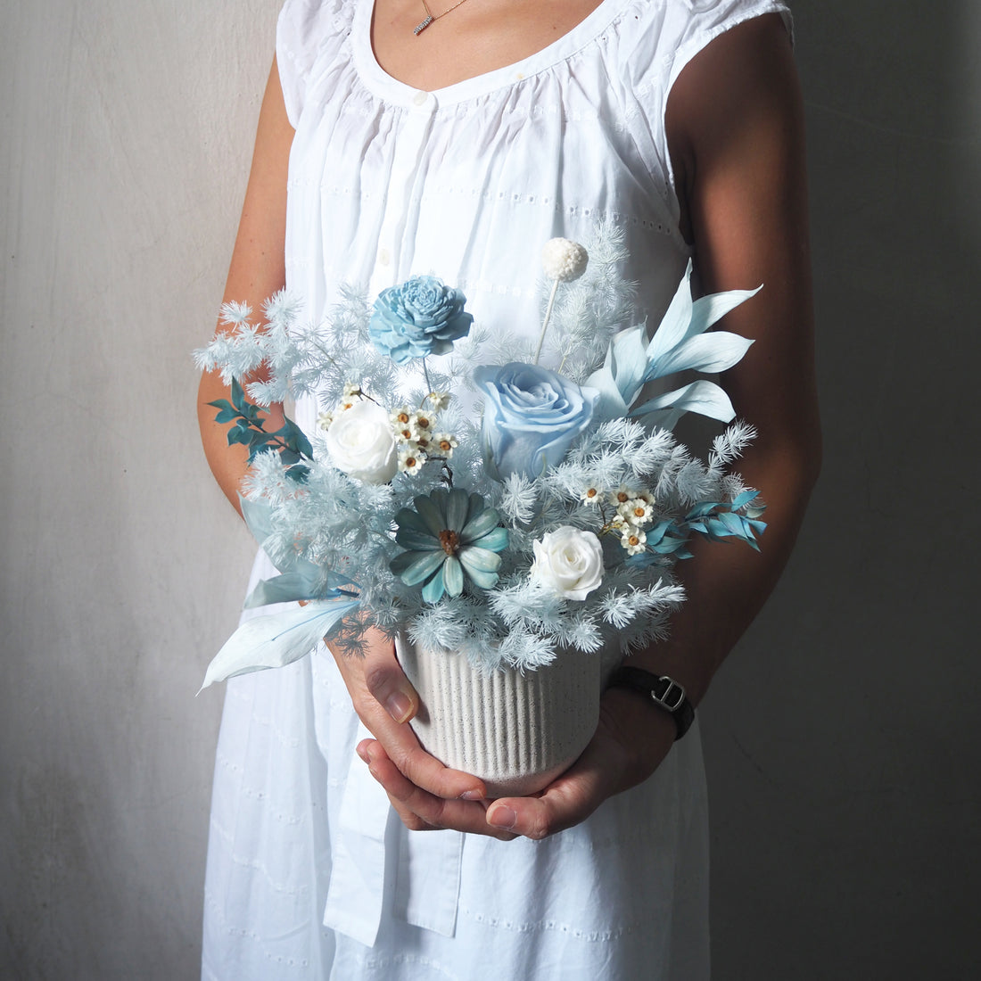 light pale blue preserved flower arrangements in white strip vase