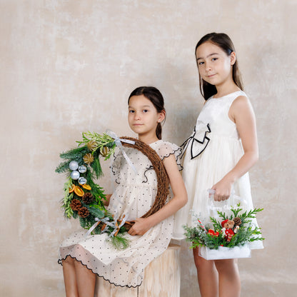 Two young girls in white dresses holding decorative wreaths against a plain background
