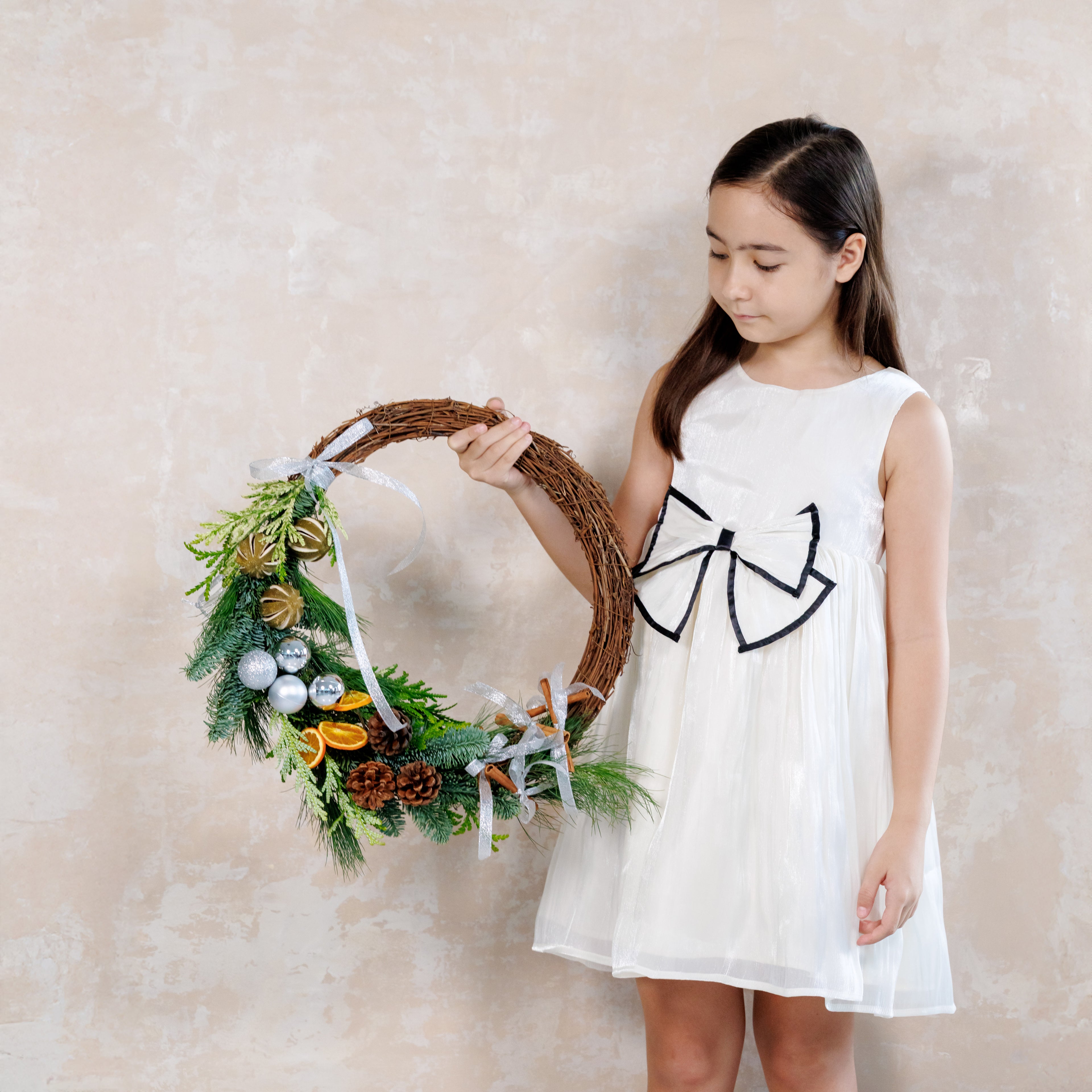 Young girl holding a decorative wreath against a plain background