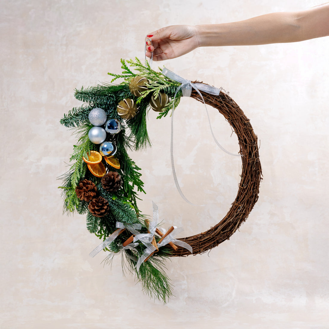 Decorative wreath with greenery, pinecones, and ornaments held by a hand on a light background