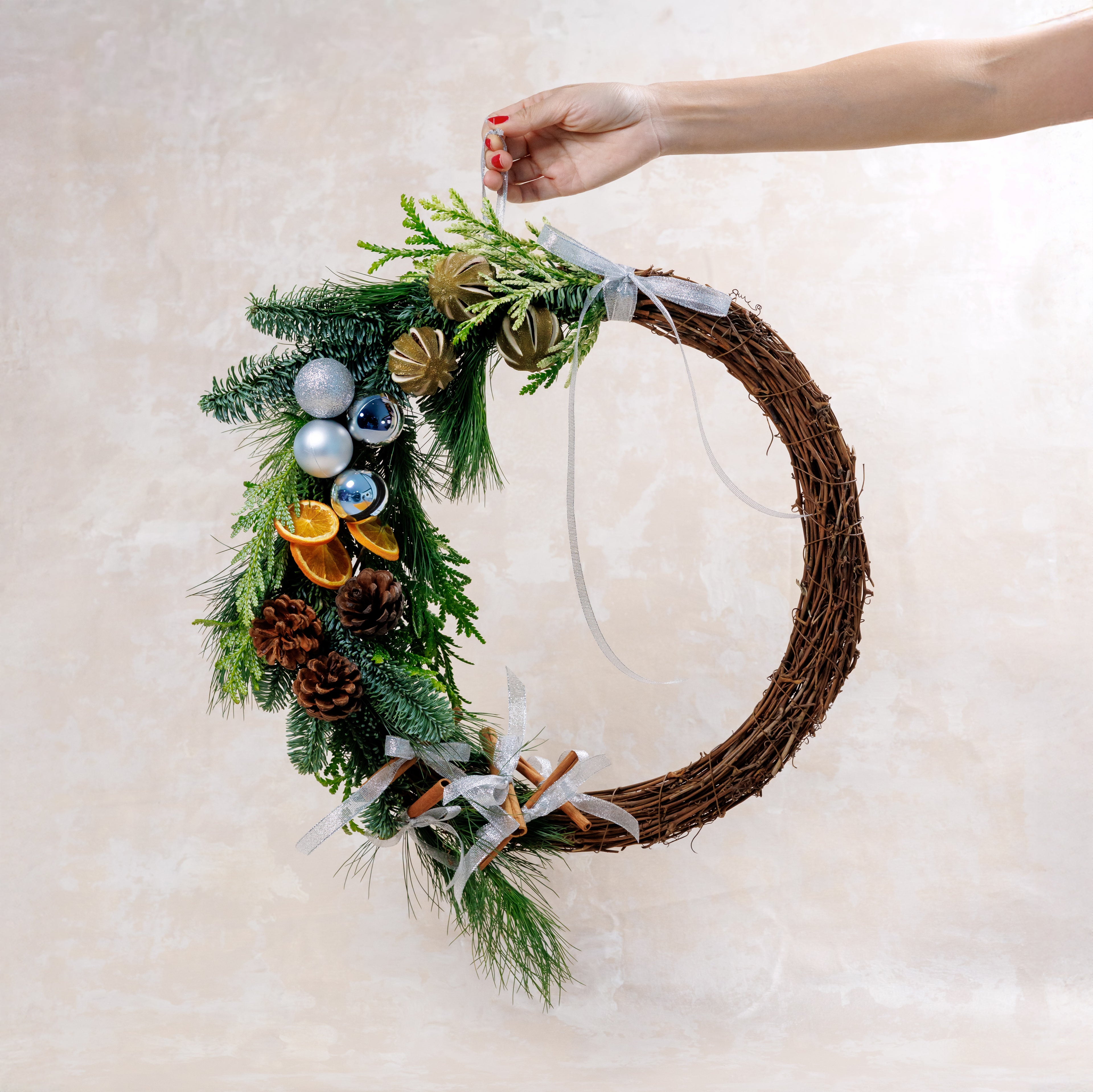Decorative wreath with greenery, pinecones, and ornaments held by a hand on a light background